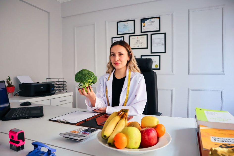 Resmi! BGN Batasi Waktu Ideal Makan MBG - Panduan Lengkap 2025 1 Female nutritionist in office holding broccoli, surrounded by fruits, promoting healthy lifestyle.