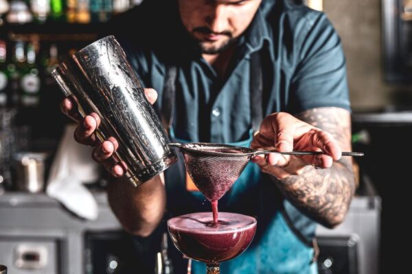A skilled bartender preparing a cocktail with a strainer and cocktail shaker in a vibrant bar setting.