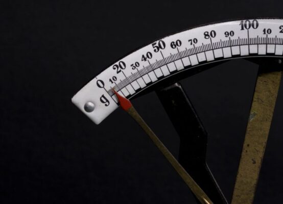 Detailed close-up image of a vintage analog weighing scale with a pointer against a black background.