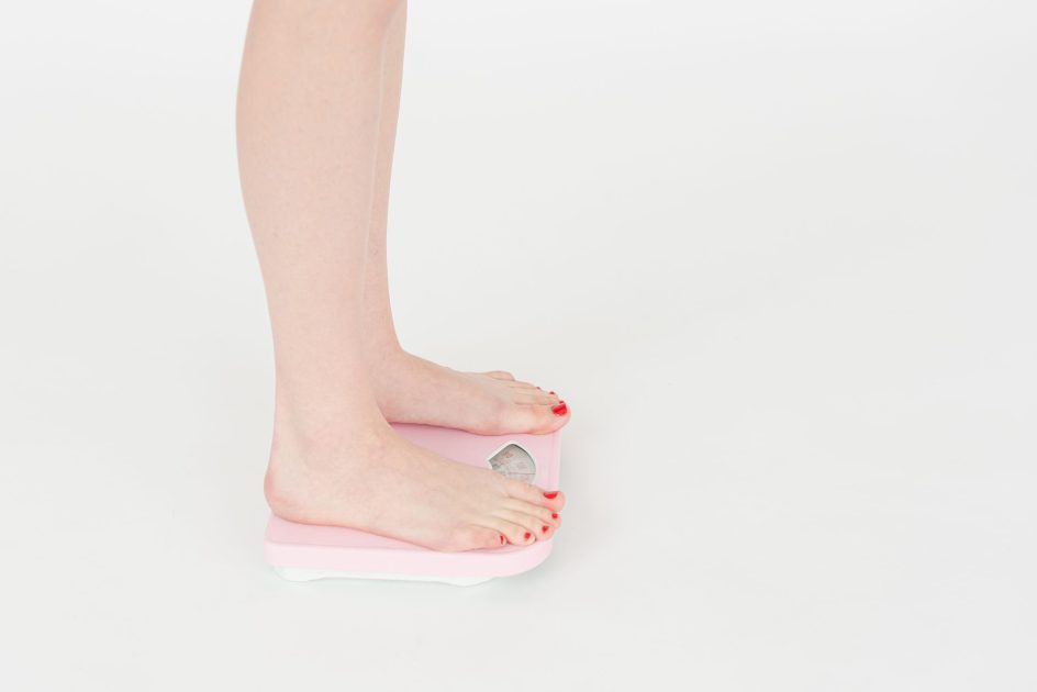 High angle side view of crop faceless female standing on scales and measuring weight on white background