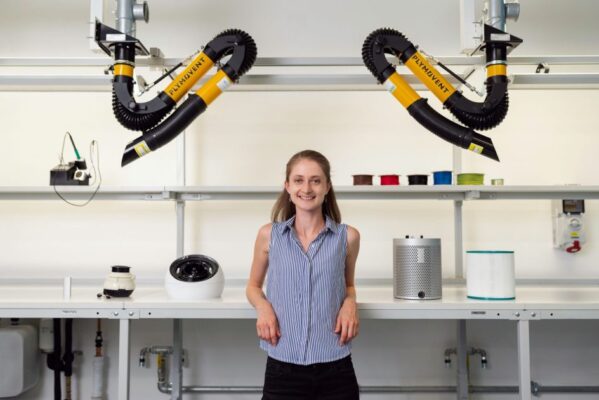 A female engineer smiling in a modern laboratory with advanced equipment and machinery.