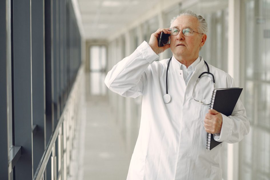 Video Pemerintah Luncurkan 25 Prodi: Solusi Krisis Dokter 3T 2025 1 Serious mature male doctor in medical uniform standing with stethoscope and notebook while talking on smartphone in clinic corridor