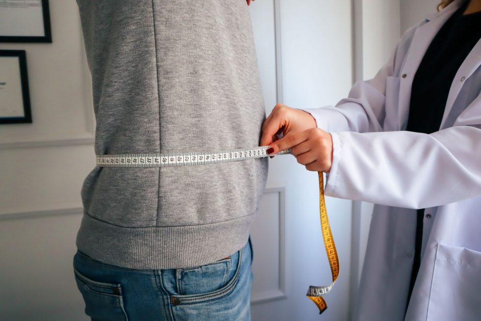 Wanita BB 300 Kg Sragen: 9 Panduan Kesehatan & Pencegahan 1 A nutritionist measuring a patient's waist using a tape in a clinical setting.