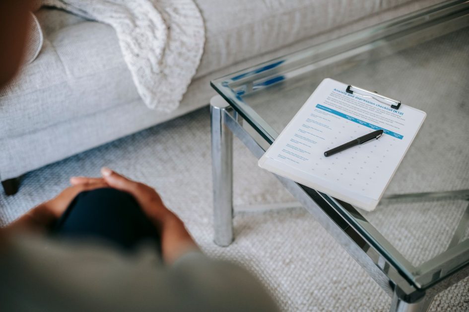 From above of blurred unrecognizable female psychologist sitting in office near table with clipboard and pen during session in office