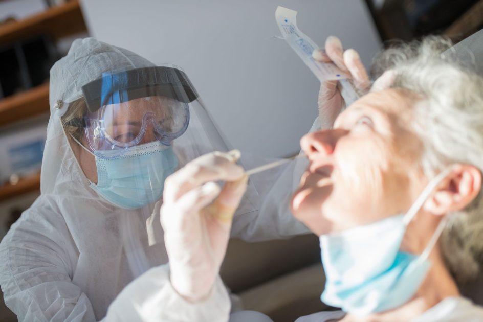 A healthcare worker in protective gear performing a COVID-19 test on a senior adult.