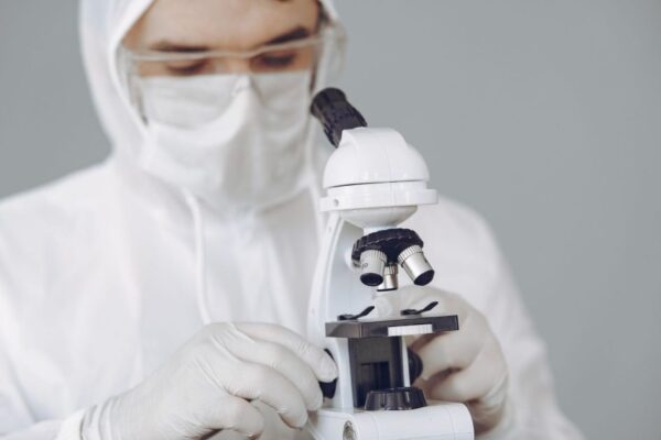 Medical professional in protective gear examining samples with microscope.