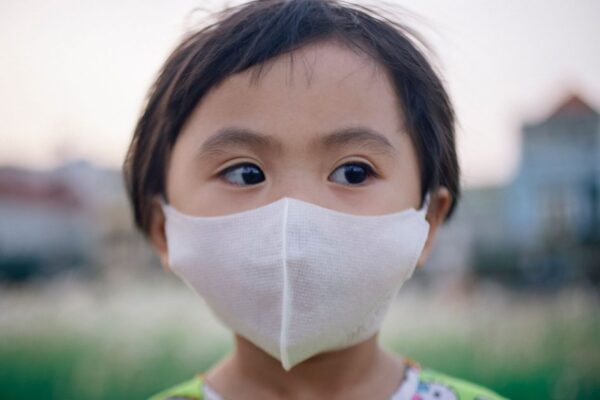 Close-up of a young child wearing a face mask outdoors, highlighting health and protection.