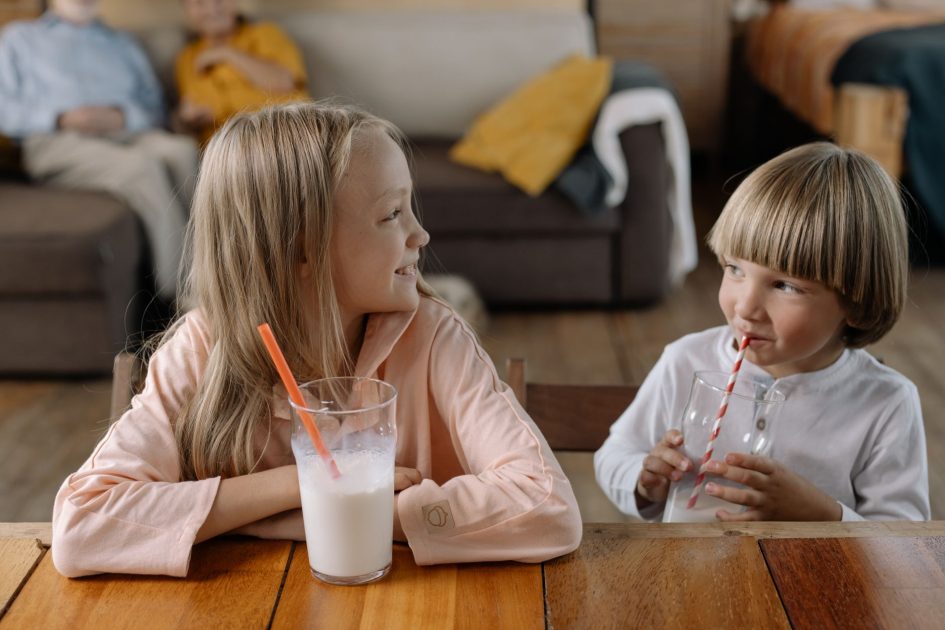 Benarkah Minum Susu Malam Hari Bikin Tidur? 7 Fakta Ilmiah 1 Two children smiling and drinking milk with straws indoors, enjoying each other's company.
