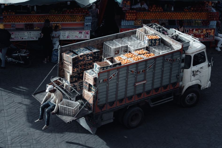 BGN Siapkan Marketplace Khusus Pengadaan: 7 Strategi Efisien 2024 1 A truck loaded with crates of oranges parked at an urban market scene during daytime.