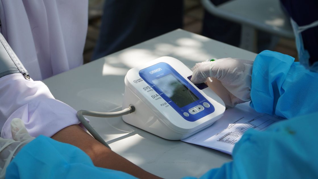 Makin Marak Hipertensi Usia Muda: 7 Panduan Pencegahan & Monitoring 1 Healthcare worker checking patient's blood pressure with a digital device outdoors.