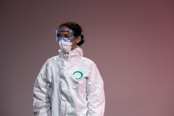 Medical professional in full protective suit with goggles and mask, studio setting.