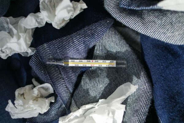 Thermometer with crumpled tissues on denim fabric, evoking themes of sickness and care.