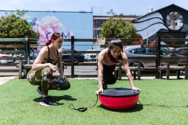 Two women exercising with a balance board outdoors. Fitness and teamwork in action.
