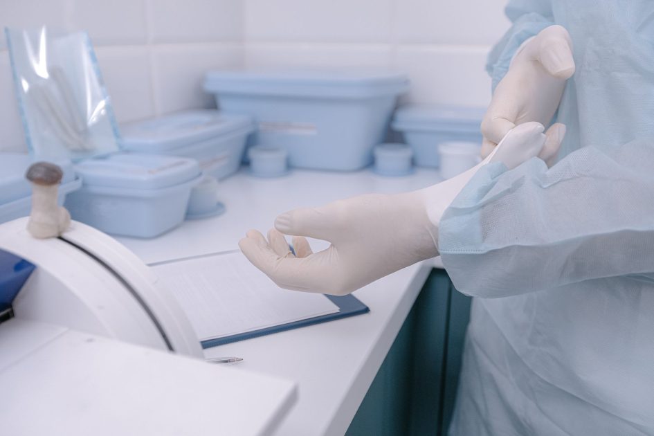 Pasien Datang Sembuh Bukan Membawa: 7 Protokol Kesehatan 1 A health worker dons gloves in a clean, sterile medical setting, emphasizing safety and hygiene.