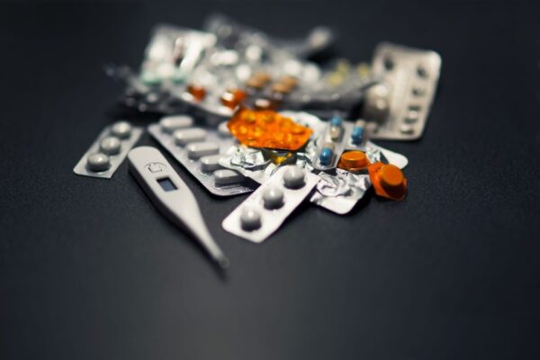 Close-up of various pills and a digital thermometer against a dark background.