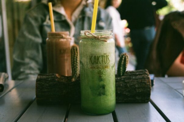Close-up of green and brown smoothies on a rustic table with twine and cactus decor, perfect for summer relaxation.
