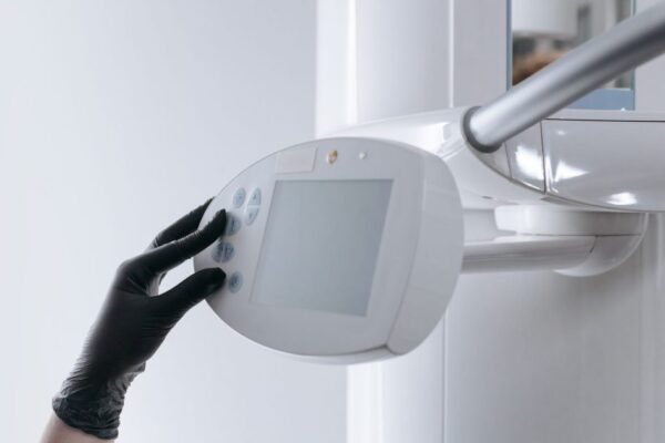 Close-up of gloved hand operating dental x-ray machine in clinical setting.