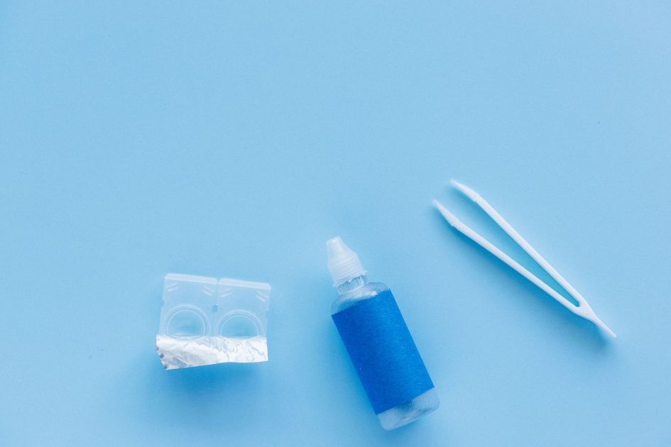 Wanita Umur 20 Alami Infeksi Mata: 7 Cara Aman Pakai Lensa Kontak 1 Flat lay of contact lenses, solution bottle, and tweezers on a blue background.
