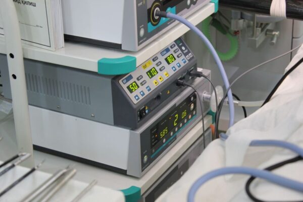 Close-up view of medical device with digital displays and cables in a hospital setting.