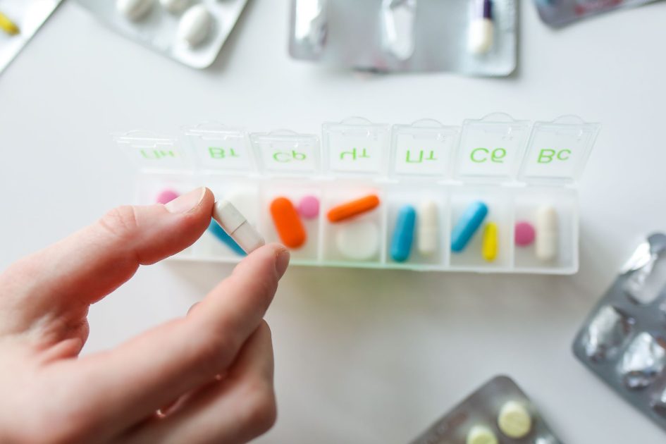BPOM Terbitkan Aturan Baru Kemasan: 7 Panduan Compliance 2026 1 Close-up of a hand selecting a pill from a weekly pill organizer, illustrating daily health and medication routines.