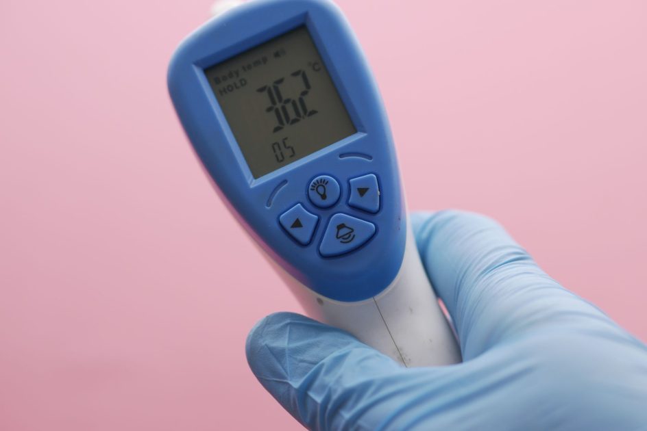 Cuaca Panas Imbas El Nino: 7 Solusi Alat Kesehatan 1 Close-up of an infrared thermometer displaying temperature, held by a gloved hand against a pink background.