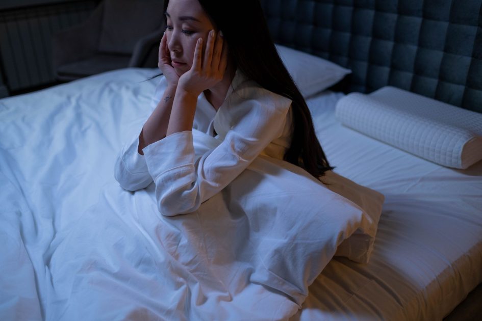 Dampak Mengerikan Keseringan Begadang: Mekanisme & Solusi 1 An Asian woman in bed at night, experiencing insomnia and loneliness, deep in thought.