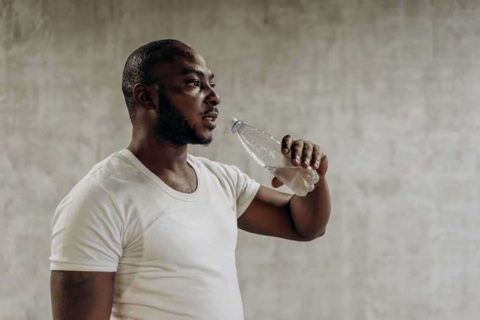 Dokter Gizi Bagikan Strategi Fueling: 7 Panduan Lengkap Agar Tidak Bonking 1 Man in white shirt drinking water after exercising indoors, promoting fitness and healthy living.