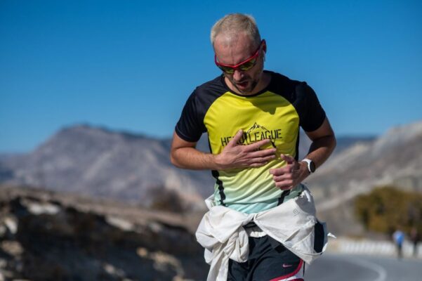 A man running on a mountain road in sunglasses and sportswear on a clear day.
