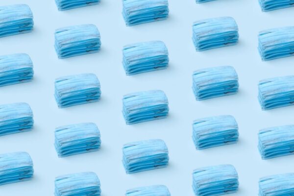Stacks of blue medical face masks arranged in a repeating pattern on a light blue background.