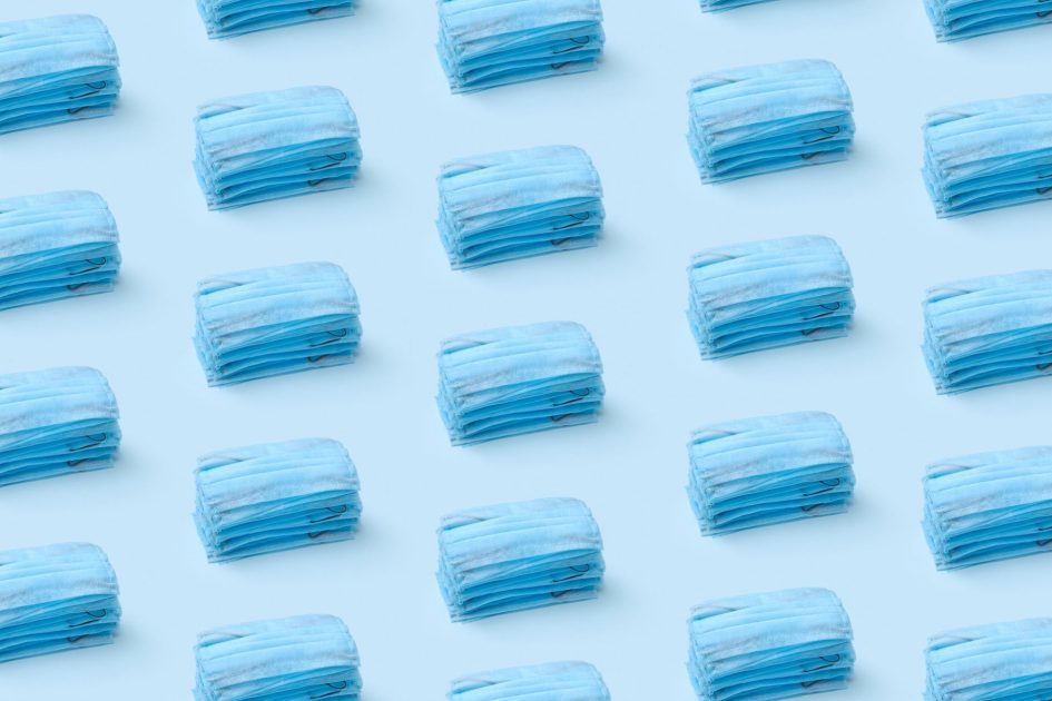 Kemenkes Siapkan 500 Ribu Masker: Panduan Lengkap 2025 1 Stacks of blue medical face masks arranged in a repeating pattern on a light blue background.
