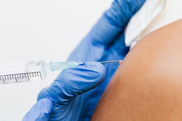 A healthcare professional administers a vaccine using a syringe in a close-up shot.