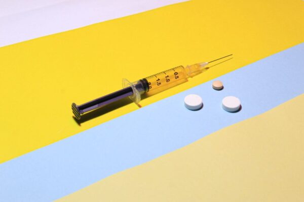 A syringe and pills on a vibrant yellow and blue background, depicting healthcare theme.