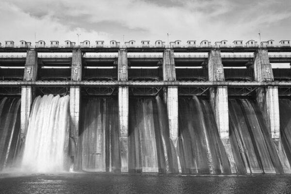 Black-and-white photo of a concrete dam with water flowing through, showcasing architectural beauty.
