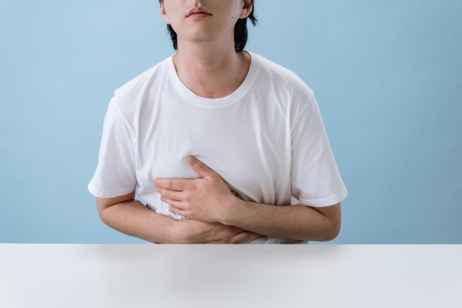 Usus Keburu Kena Corak Kulit: 7 Panduan Pulih & Pencegahan 2025 1 An adult man in a white shirt holds his stomach, indicating pain and discomfort, with a light blue background.