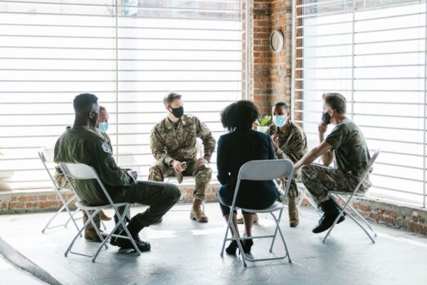 A group therapy session with soldiers in military uniform and face masks indoors.