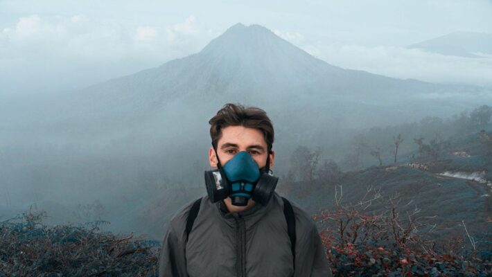 A man with a respirator mask stands in a misty mountain landscape, suggesting environmental awareness and adventure.